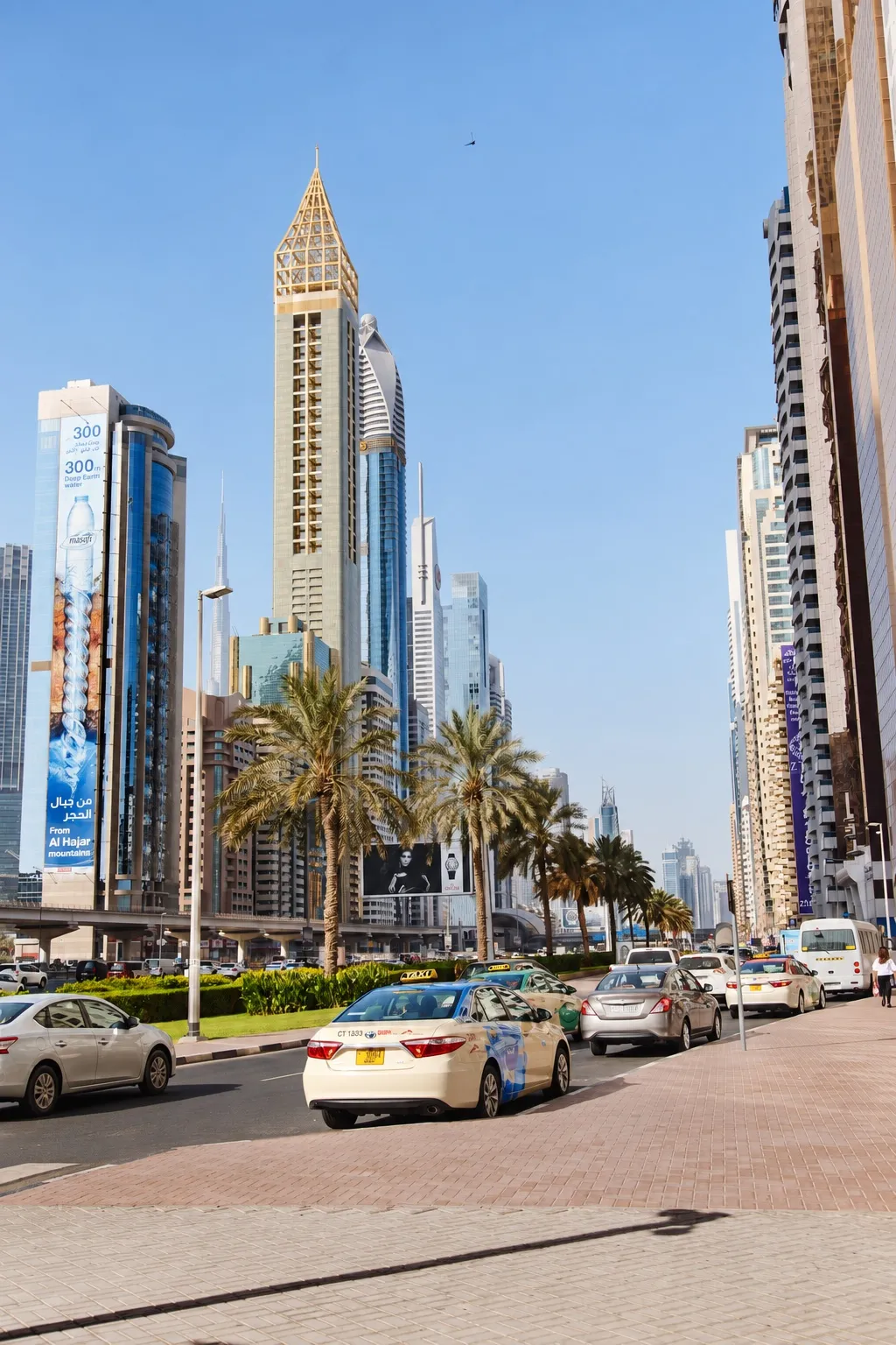 Taxis and palm trees along a Dubai street beneath high-rise buildings.