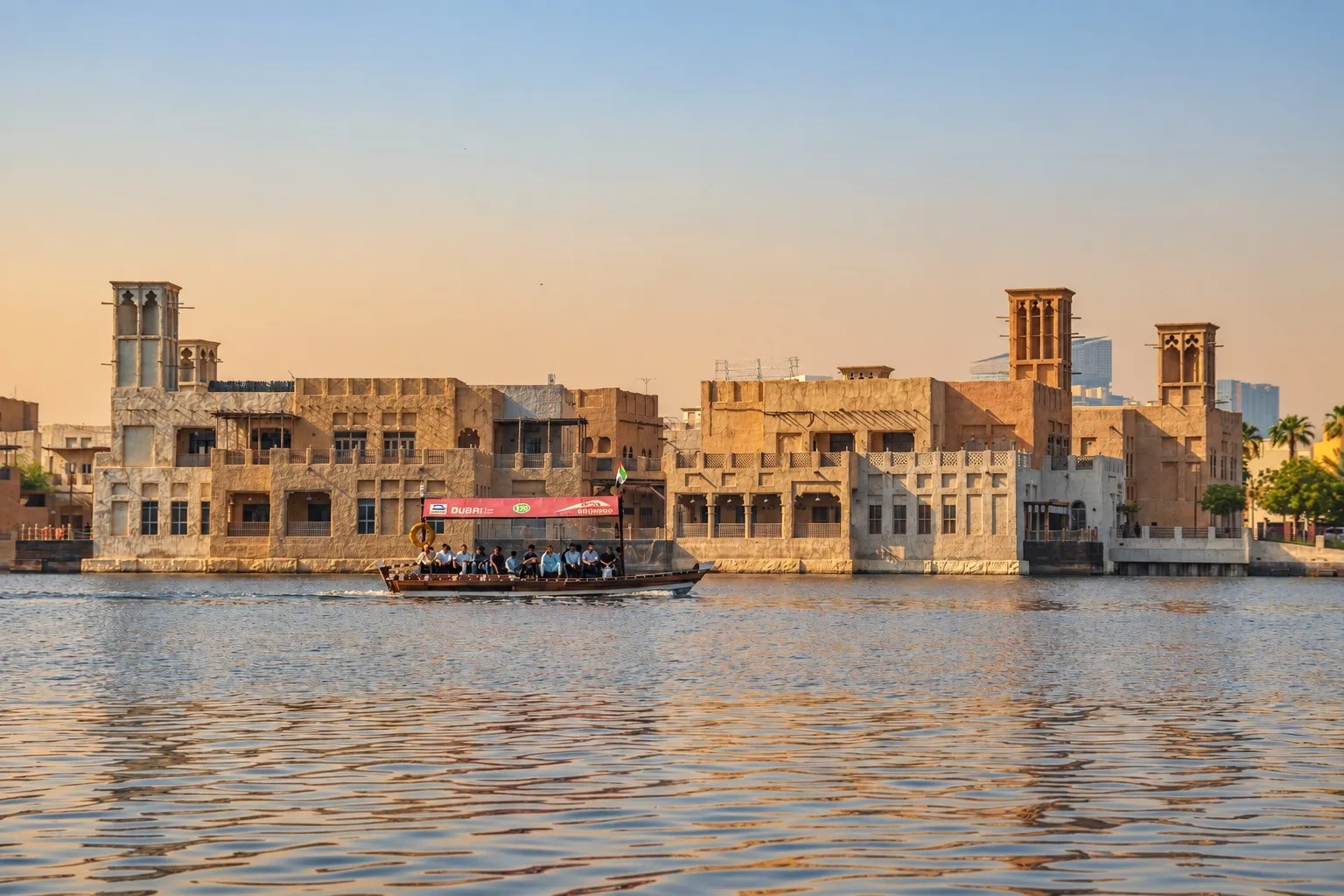 An abra carrying passengers crosses Dubai Creek in front of wind-tower buildings.