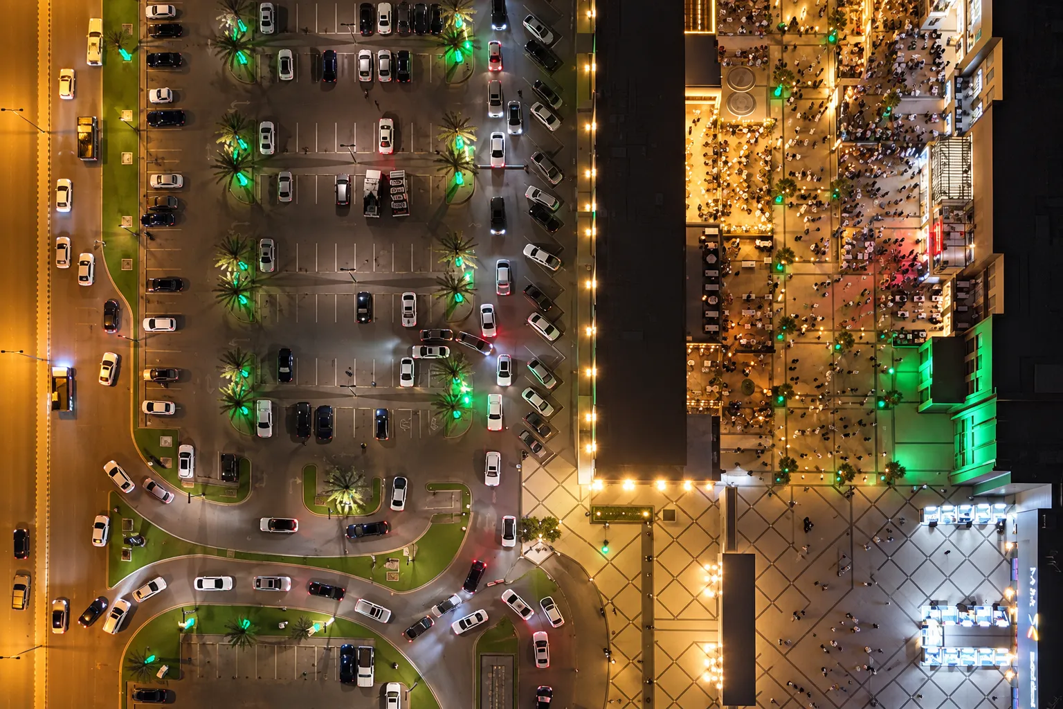 Overhead night view of a Riyadh parking area beside a busy dining precinct.
