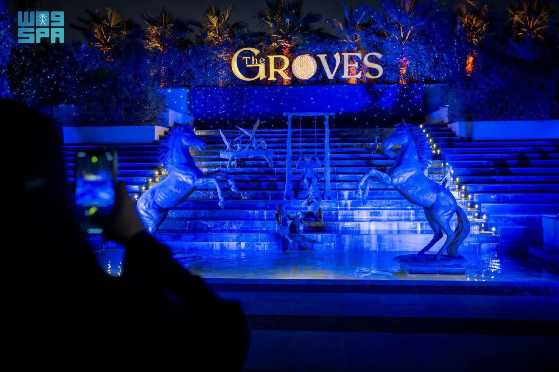The Groves sign and horse sculptures glow blue beside a stepped water feature at Riyadh Season