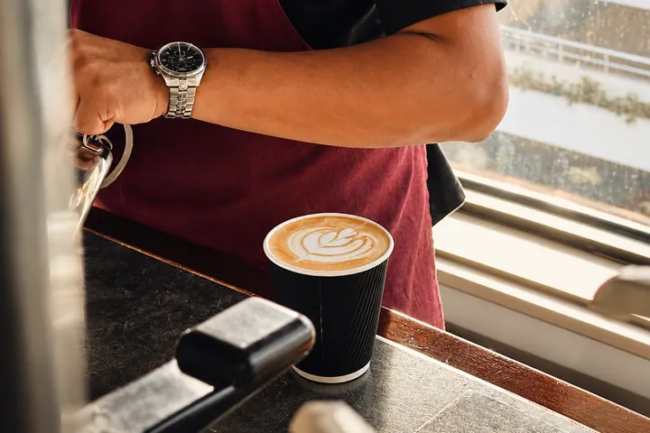A barista at a Riyadh coffee counter beside a freshly poured latte