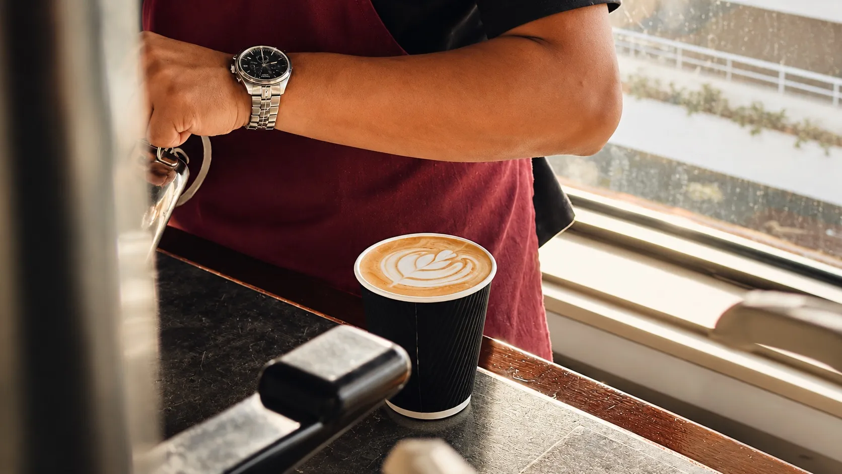 A barista at a Riyadh coffee counter beside a freshly poured latte